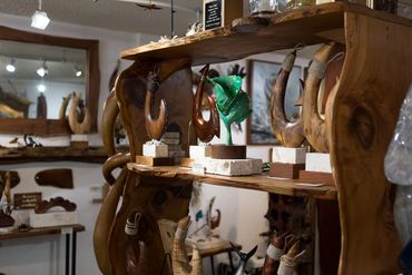 Carved wood fish hook sculptures and marine-inspired artwork displayed on rustic wood shelving.