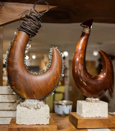 Hand-carved wood fish hook sculptures with decorative lashing displayed on stone and wood bases.