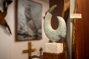 Fish hook sculpture with a wrapped tip displayed on a fossil coral base inside Wirth Gallery.