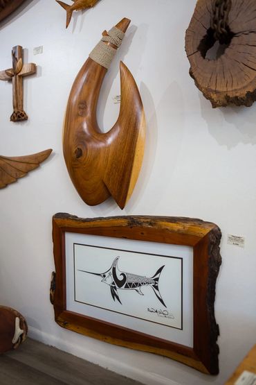 Large carved wood fish hook sculpture displayed above framed marlin artwork inside Wirth Gallery.