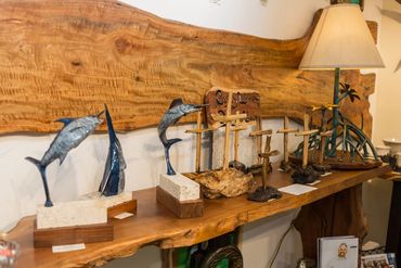 Billfish sculptures and handcrafted coastal artwork displayed on a live-edge wood shelf.