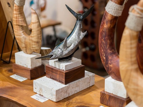 Marlin sculpture among hand-carved wood fish hook sculptures on fossil coral and wood bases.
