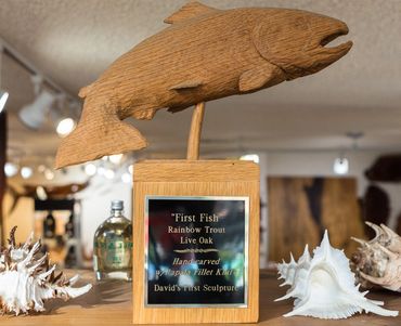Hand-carved live oak rainbow trout sculpture titled First Fish displayed on a wooden base.