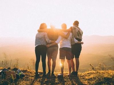 Group of happy friends stands and hugs against sunset mountains