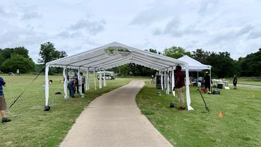 People setting up tents at an outdoor event on a golf turnament course.
