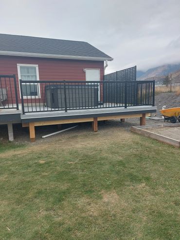 Backyard deck with black railing, hot tub, and mountain view under cloudy sky.