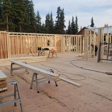 Wooden frame of a house under construction surrounded by trees.
