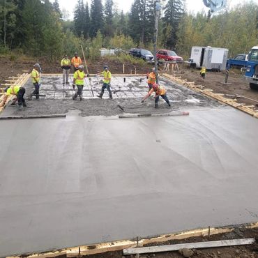 Construction workers pouring and smoothing concrete on a foundation slab outdoors.