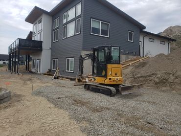 Modern house under construction with excavator and gravel driveway.