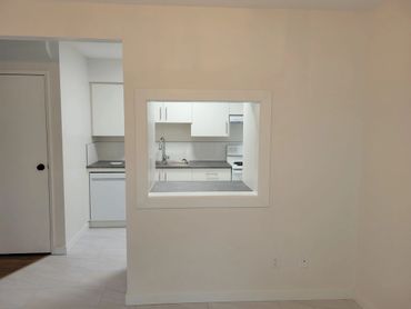 Modern kitchen seen through a pass-through window in a beige wall.