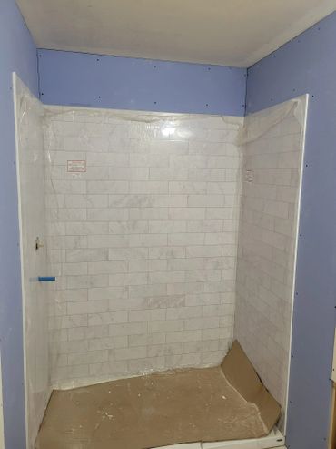 Partially installed shower with protective plastic and cardboard on the floor.