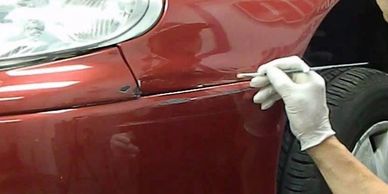 Man is using a paint brush to touch up paint scratches on the front bumper of a red car.