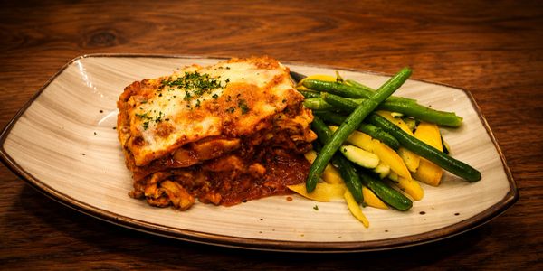Lasagna with green and yellow beans on a white plate.