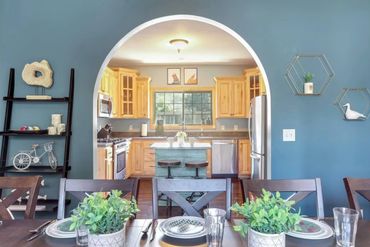 Cozy dining area with blue walls opening to a warm wooden kitchen through an arched doorway.