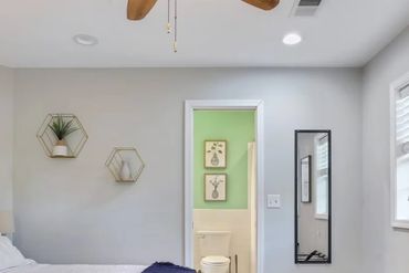 Bright bedroom with white bedding, blue throw, and adjoining bathroom with green walls.