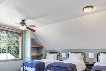 A bright bedroom with four single beds and blue blankets near a large window.