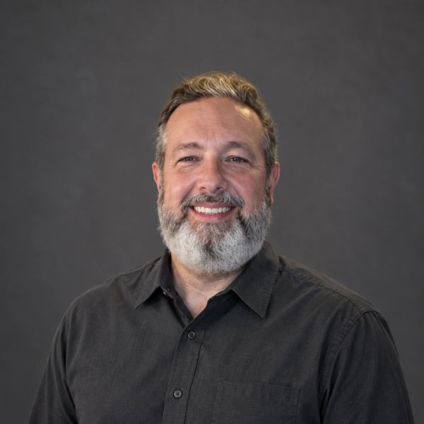 Smiling man with beard and dark shirt.