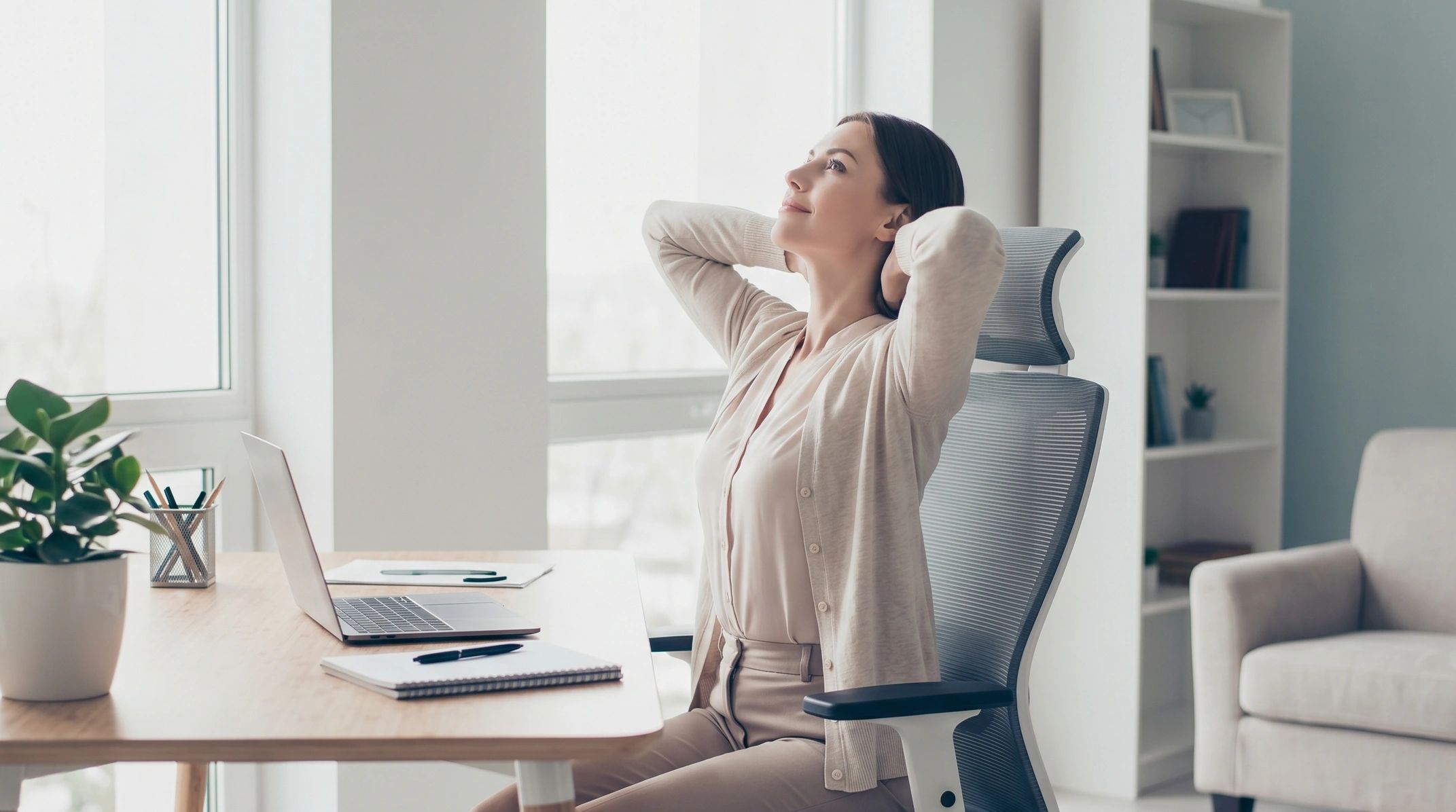 Woman relaxing at her desk with a laptop and notebook.
