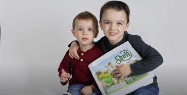 Two boys smiling, the older one holding a Shell children's book.