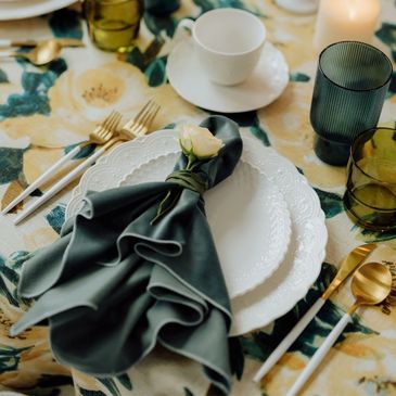 Elegant table setting with white plates, gold cutlery, and a dark green napkin adorned with a small flower.