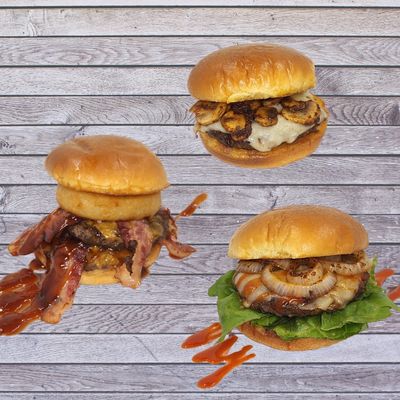 Three gourmet burgers with various toppings on wooden background.