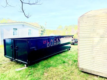 A large black dumpster with "BLACKWATER DUMPSTER" text on the side on green grass.