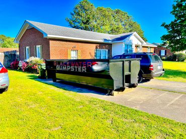 A large Blackwater Dumpster on a driveway in front of a brick house.