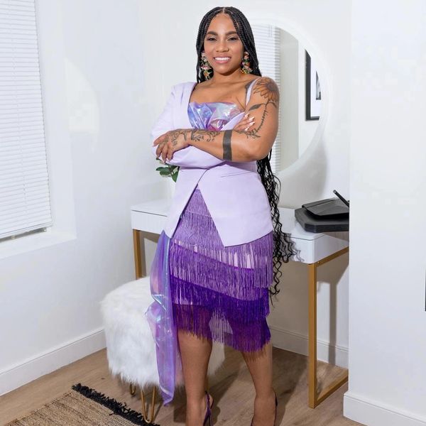 Woman in a stylish purple fringe dress with braided hair and tattoos, posing confidently indoors.