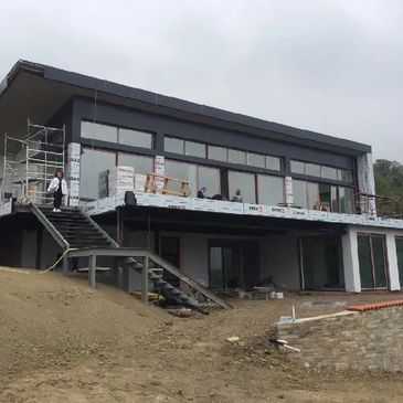Modern house under construction on a sloped plot with scaffolding and workers.