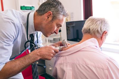 Doctor examining an elderly woman's skin with a dermatoscope.