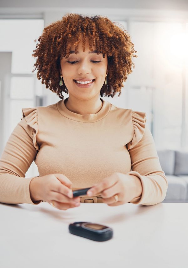 Smiling woman checking her glucose monitor in a bright room.