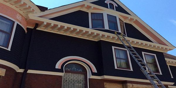Victorian-style house with dark siding and peach trim under a clear blue sky.