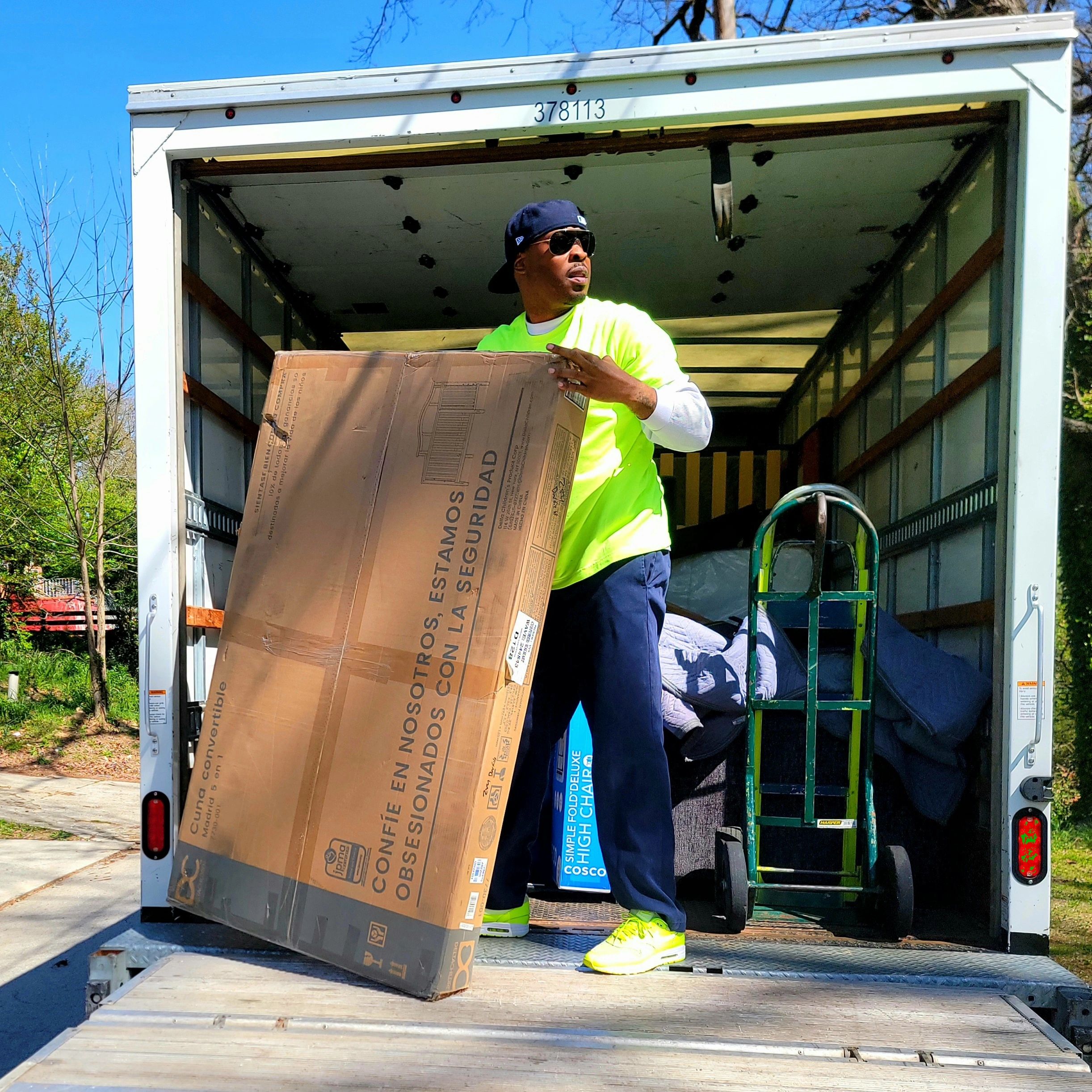 Mover standing on liftgate of moving truck holding box vertically wearing safety green shirt