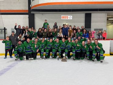 Ice hockey team and fans celebrate with a trophy on the rink.