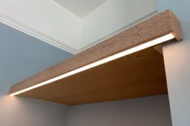 Wooden shelf with integrated LED light mounted on a wall corner.