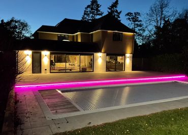 Modern house with illuminated pool area and pink LED lighting at dusk.