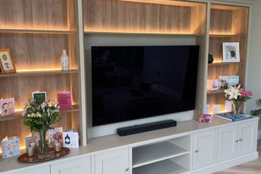 Modern entertainment unit with TV, flowers, and greeting cards on illuminated shelves.