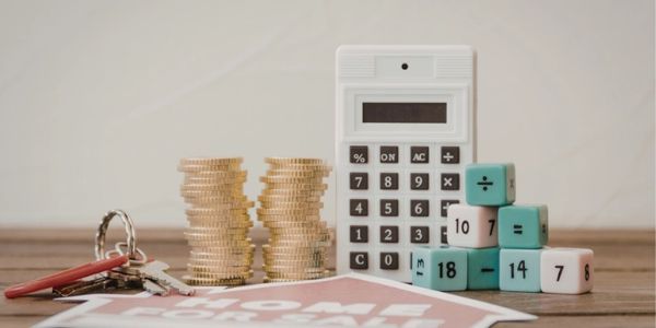 Calculator, stacked coins, dice with math symbols, keys, and a loan approval paper on a table.