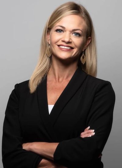 Confident woman in black blazer smiling with arms crossed.