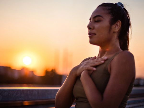 woman at sunrise holding her heart breathing deep