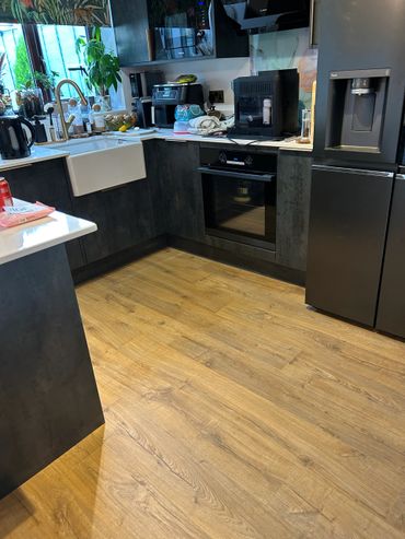 Modern kitchen with wooden flooring and black appliances.