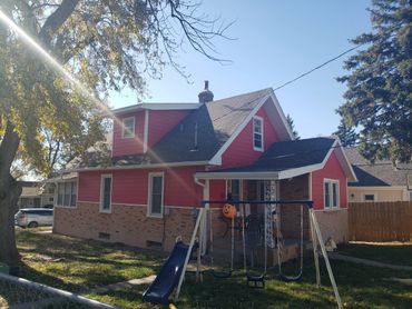 A red and brick house with a swing set and slide in the front yard.