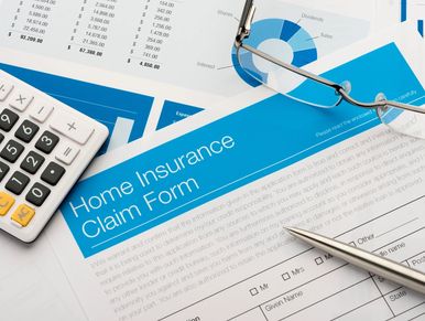 Home insurance claim form with pen, calculator, and glasses on financial documents.