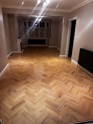 Empty room with polished herringbone wooden floor and neutral walls.