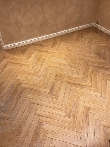 Newly installed herringbone wooden floor in an empty room with beige walls.