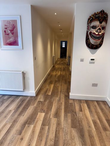 A hallway with wooden flooring, a framed artwork, and a decorative mask on the wall.