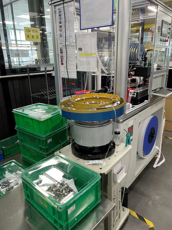 Industrial machine sorting small metal components into green bins.