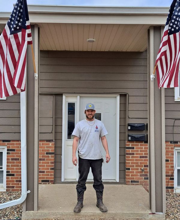 Man standing on a porch between two American flags.