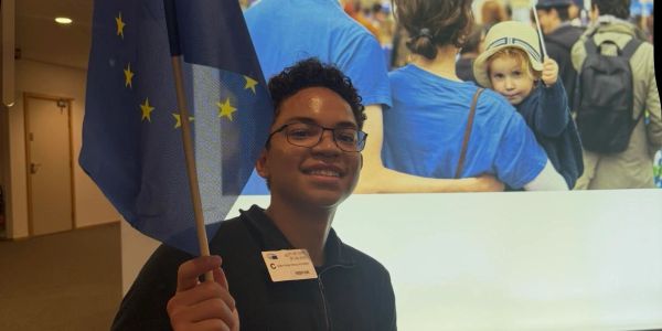 Person smiling holding a European Union flag indoors.