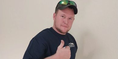 Man giving a thumbs up while wearing a cap and sunglasses on his head.